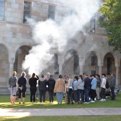Students look at an Elder with smoke rising in the UQ Great Court
